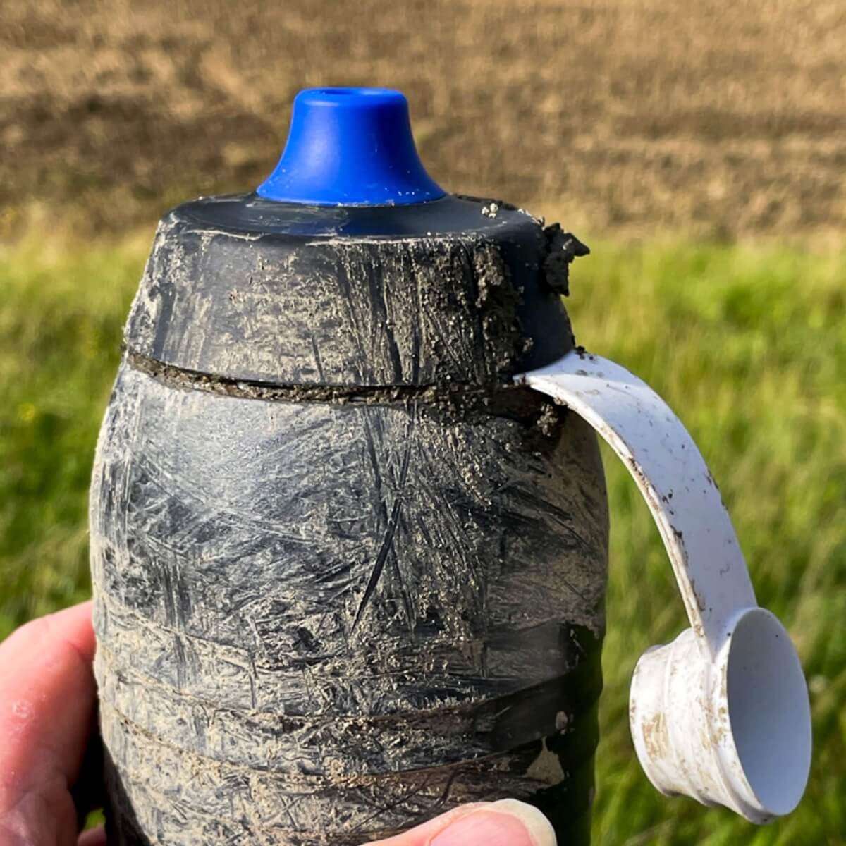 Eine mit Schlamm verschmierte schwarze Keego Trinkflasche mit offenem Verschluss, der den Mundstuck sauber gehalten hat