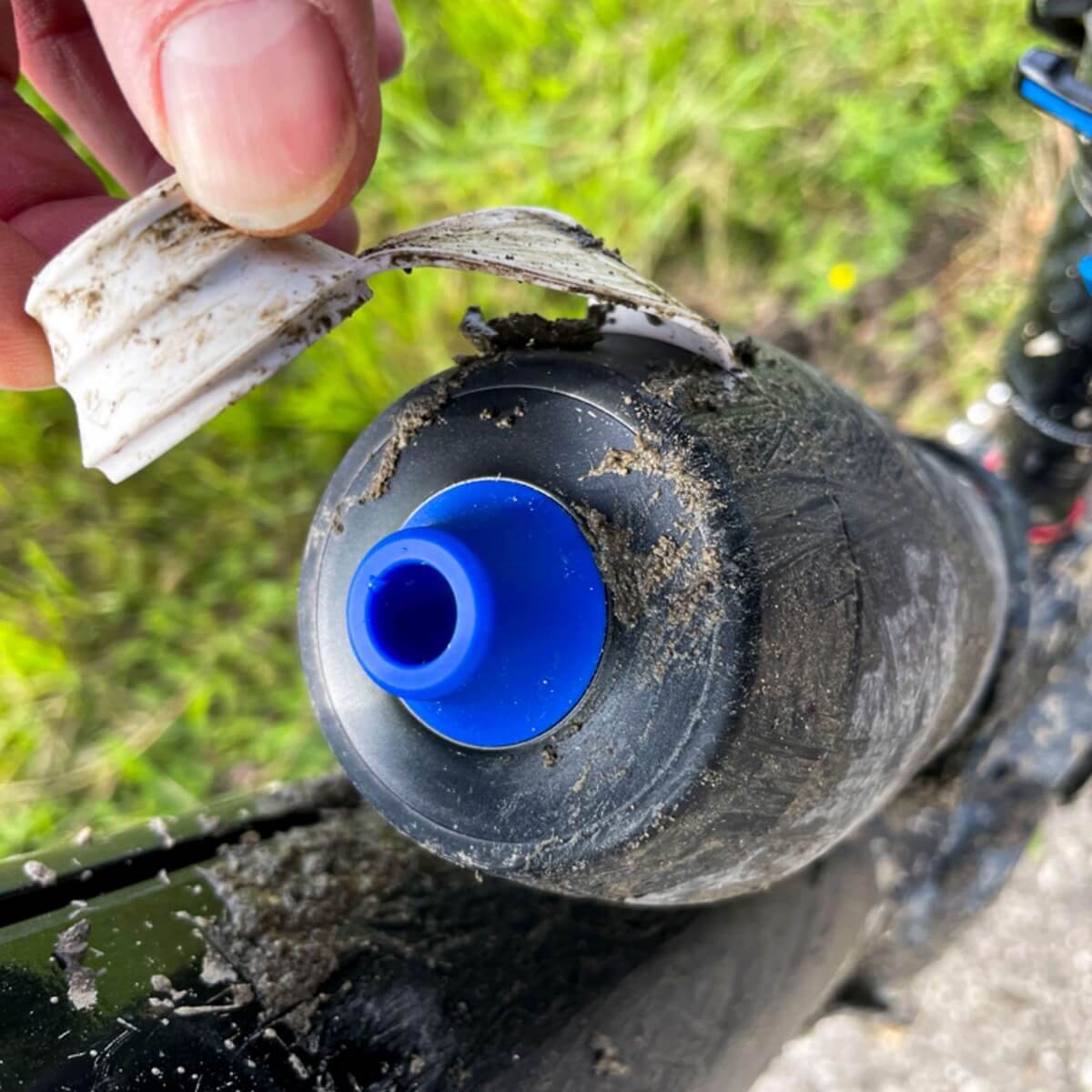Ein Radfahrer hat die Staubkappe einer Flasche geöffnet, die mit Schlamm beschmiert ist, aber das Mundstück ist sauber