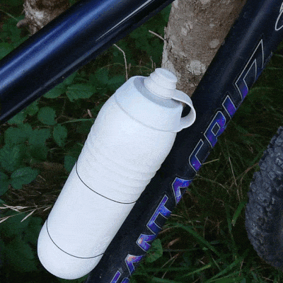 Ein Radfahrer nimmt eine weisse Keego Trinkflasche aus dem Flaschenhalter, öffnet und verschließt den DustCap