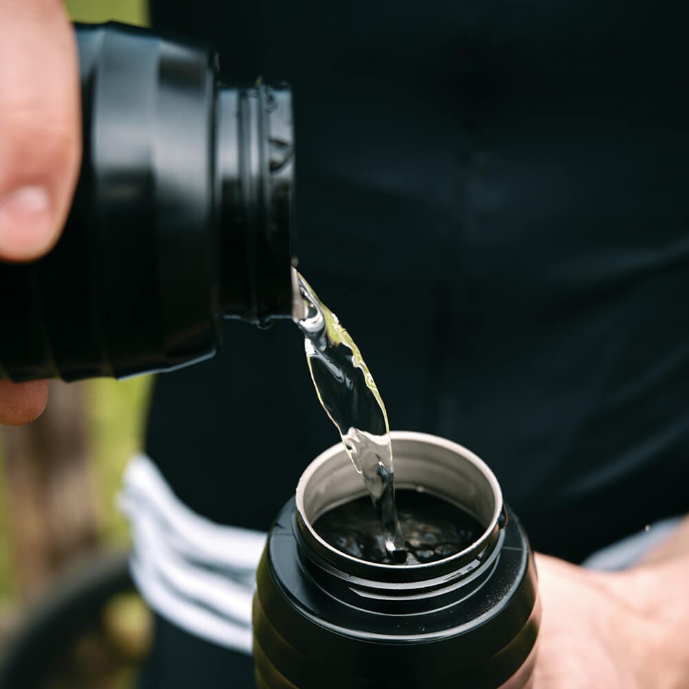 Ein Radfahrer gießt Wasser von einer schwarzen Fahrradflasche TWISTxKEEGO 0.6L in eine andere